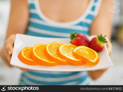 Closeup on plate with strawberry and orange in hand of woman