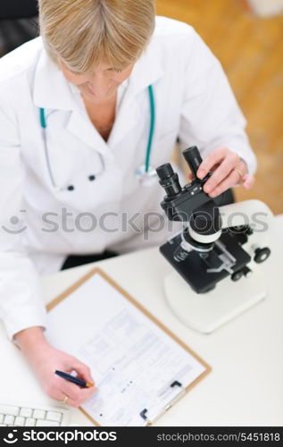 Closeup on researcher working with microscope and making notes in clipboard