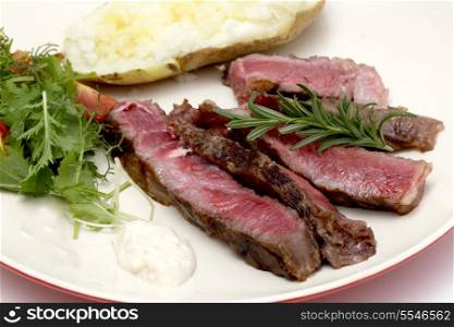 Closeup on slices of grilled gourmet wagyu rib-eye steak served with horseradish sauce, a baked potato and a fresh green salad