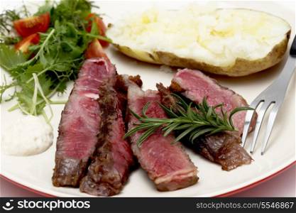Closeup on slices of grilled gourmet wagyu rib-eye steak served with horseradish sauce, a baked potato and a fresh green salad