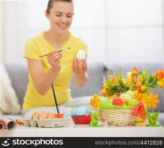 Closeup on table with Easter decoration and woman drawing on egg in background