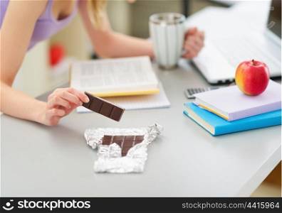 Closeup on teenage girl eating chocolate while studying in kitchen