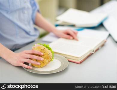 Closeup on teenage girl with sandwich and book in kitchen
