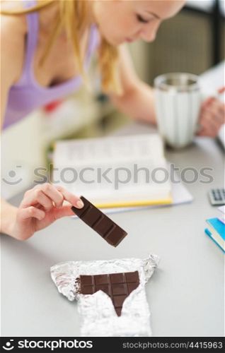 Closeup on teenager girl eating chocolate while studying in kitchen