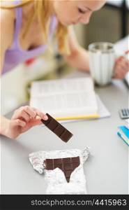 Closeup on teenager girl eating chocolate while studying in kitchen