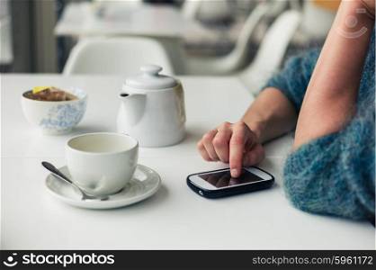 Closeup on the hands of a young woman as she is using her smartphone while having a cup of tea in a cafe