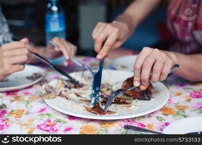 Closeup on two women&rsquo;s hands as they are cutting a fish in a restaurant
