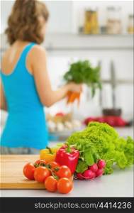 Closeup on vegetables on cutting board and young housewife in background