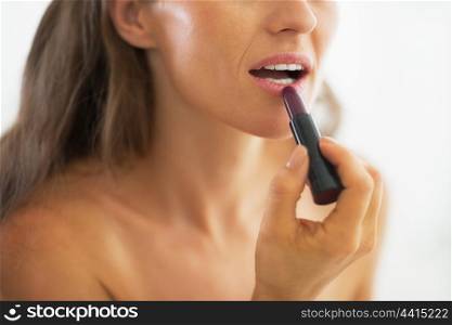 Closeup on woman applying lipstick in bathroom