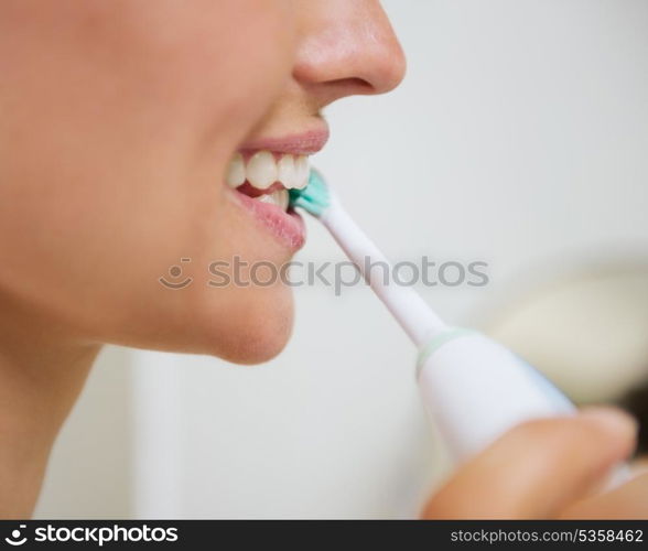 Closeup on woman brushing teeth with electric toothbrush