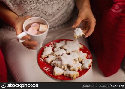 Closeup on woman eating Christmas cookie and drinking hot chocolate with marshmallows