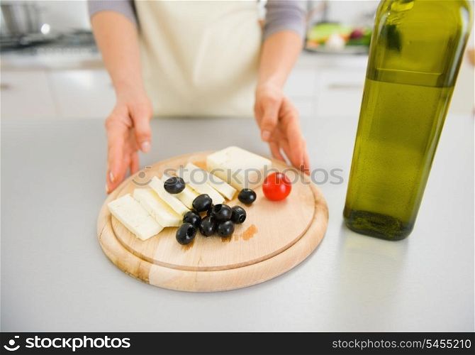 Closeup on young housewife giving olives and cheese on cutting board