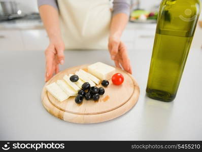 Closeup on young housewife giving olives and cheese on cutting board