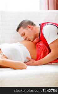 Closeup on young husband kissing his pregnant wifes tummy&#xA;