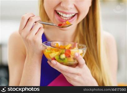 Closeup on young woman eating fresh fruits salad in kitchen