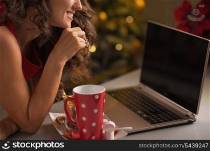 Closeup on young woman having christmas cookies with cup of hot chocolate and usign laptop