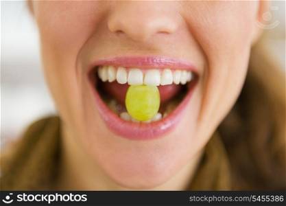 Closeup on young woman holding grape in mouth