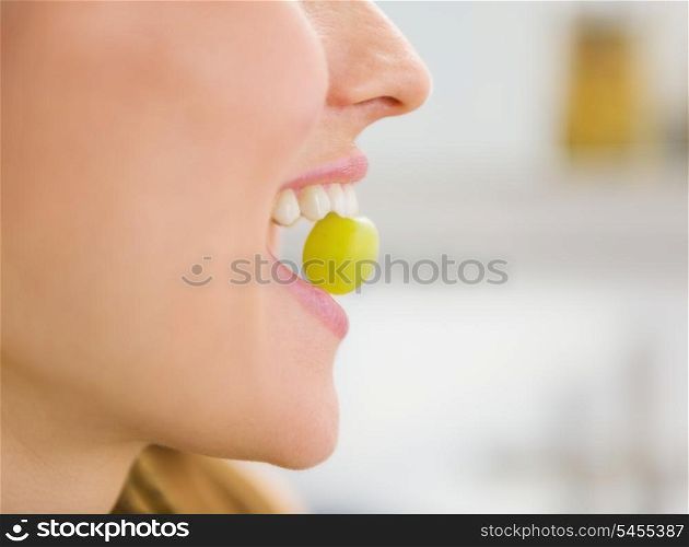 Closeup on young woman holding grape in mouth