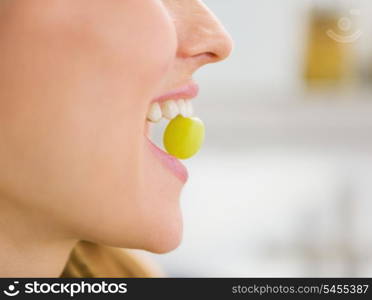 Closeup on young woman holding grape in mouth