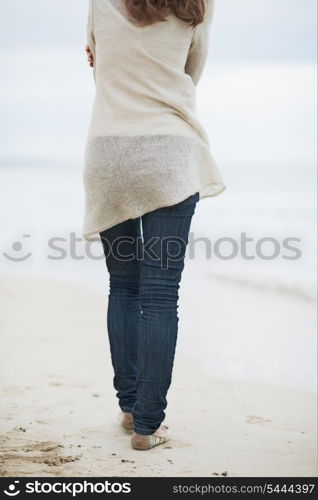 Closeup on young woman in sweater walking on lonely beach . rear view