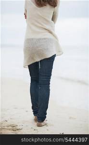 Closeup on young woman in sweater walking on lonely beach . rear view