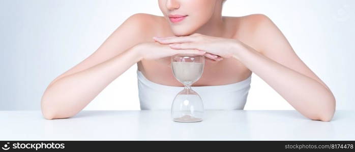 Closeup personable model holding hourglass in beauty concept of anti-aging skincare treatment. Young girl portrait with perfect smooth clean skin and flawless soft makeup in isolated background. Closeup personable beautiful woman with hourglass as anti-aging skincare concept