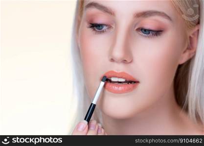 Closeup personable young woman with flawless healthy skin and natural makeup putting fashion glossy lipstick on her lip with lip brush in isolated background. Facial cosmetic makeup in process.. Closeup personable young woman putting alluring fashion glossy lipstick.