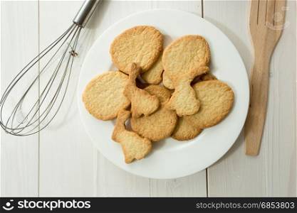 Closeup photo from above of dish with cookies and kitchen utensils on white desk