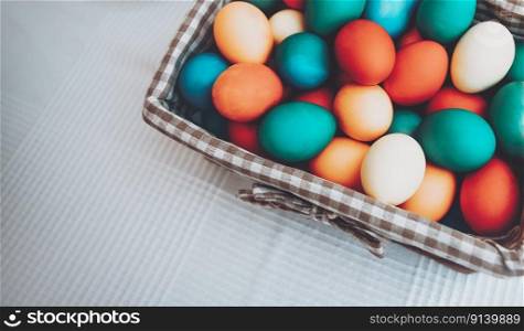 Closeup photo of a basket with colorful Easter eggs. Coloring eggs. Food border over white table background. Traditional symbol of a great Christian holiday.. Festive basket with colorful Easter eggs