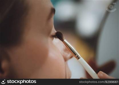 Closeup photo of a beautiful woman doing her makeup at home. Applying eye shadow. Getting ready for night out. Beauty and style of a young lady.. Woman doing her makeup at home