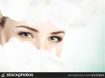 Closeup photo of a beautiful woman with gentle white orchid flowers over face, natural floral cosmetics, day spa in the beauty salon