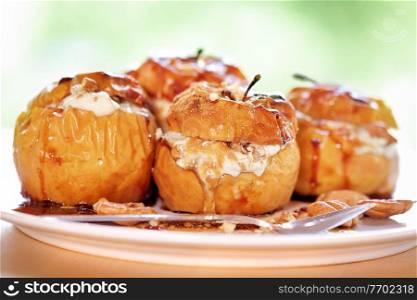 Closeup photo of a tasty baked apples stuffed with cheese cream, flavored with cinnamon, nuts and honey, served on the plate with a silver spoon, healthy nutrition, delicious fruit dessert