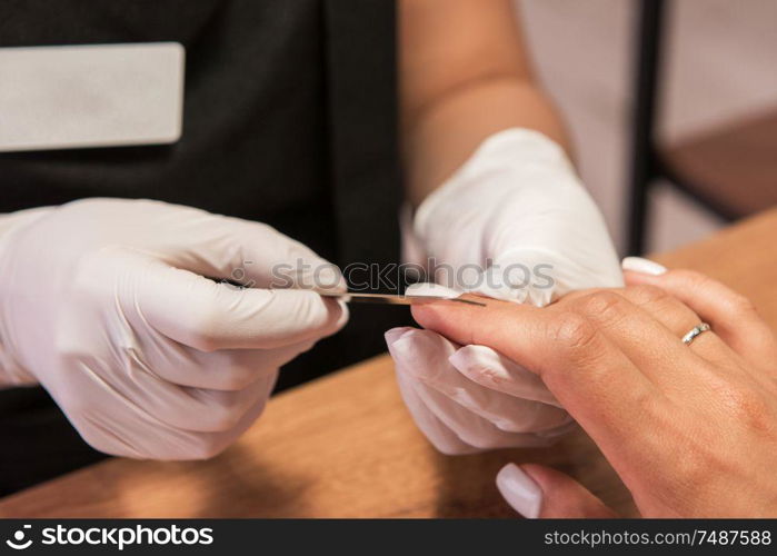 Closeup photo of a woman in a nail salon receiving a manicure by a beautician with nail file.. Woman in a nail salon