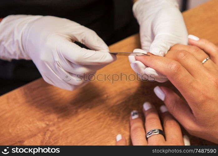 Closeup photo of a woman in a nail salon receiving a manicure by a beautician with nail file.. Woman in a nail salon