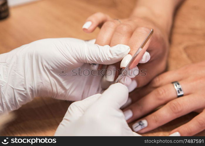 Closeup photo of a woman in a nail salon receiving a manicure by a beautician with nail file.. Woman in a nail salon