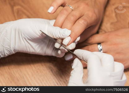 Closeup photo of a woman in a nail salon receiving a manicure by a beautician with nail file.. Woman in a nail salon