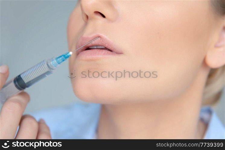 Closeup Photo of a Women&rsquo;s Face Part with Syringe over Gray Background. Lip Augmentation Procedure. Nice Female in a Beauty Clinic.. Lip Augmentation in The Clinic