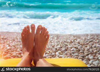 Closeup photo of a women&rsquo;s feet with nice pedicure lying down on stony seashore, conceptual photo of summer vacation on the beach