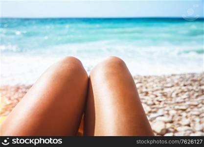 Closeup photo of a women&rsquo;s legs lying down on stony seashore, body part, young female with pleasure taking sunbath, conceptual photo of summer vacation on the beach