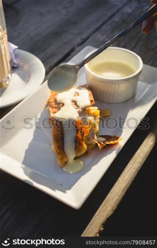 Closeup photo of apple strudel with vanilla sauce on wooden table