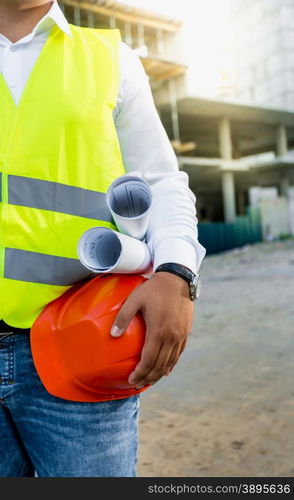 Closeup photo of architect posing on building site with hardhat and blueprints