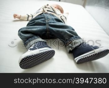 Closeup photo of baby boy feet in jeans and sneakers lying on bed