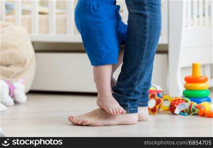 Closeup photo of baby&rsquo;s feet standing in front of mothers feet on floor