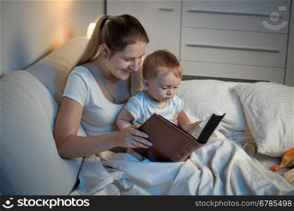 Closeup photo of beautiful smiling mother telling story to her baby at bed before going to sleep