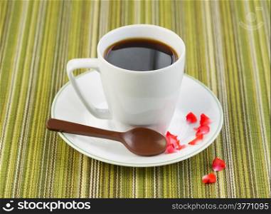 Closeup photo of black coffee, in small cup, with chocolate spoon, red rose petals on saucer