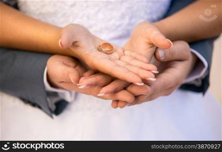 Closeup photo of bride and groom holding golden wedding rings on hands