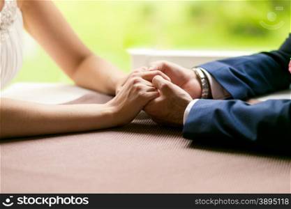 Closeup photo of bride and groom holding hands on table at restaurant