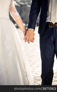 Closeup photo of bride and groom holding hands outdoor