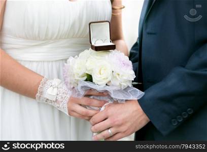 Closeup photo of bride and groom holding wedding bouquet with golden rings
