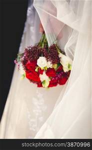 Closeup photo of bride holding wedding bouquet of red and white roses